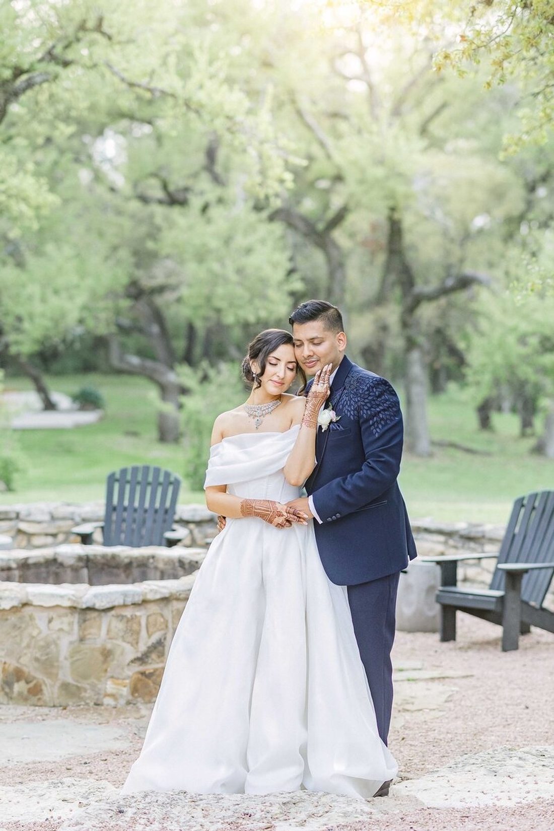Bride leaning against the groom in front of a sun-dappled oak grove