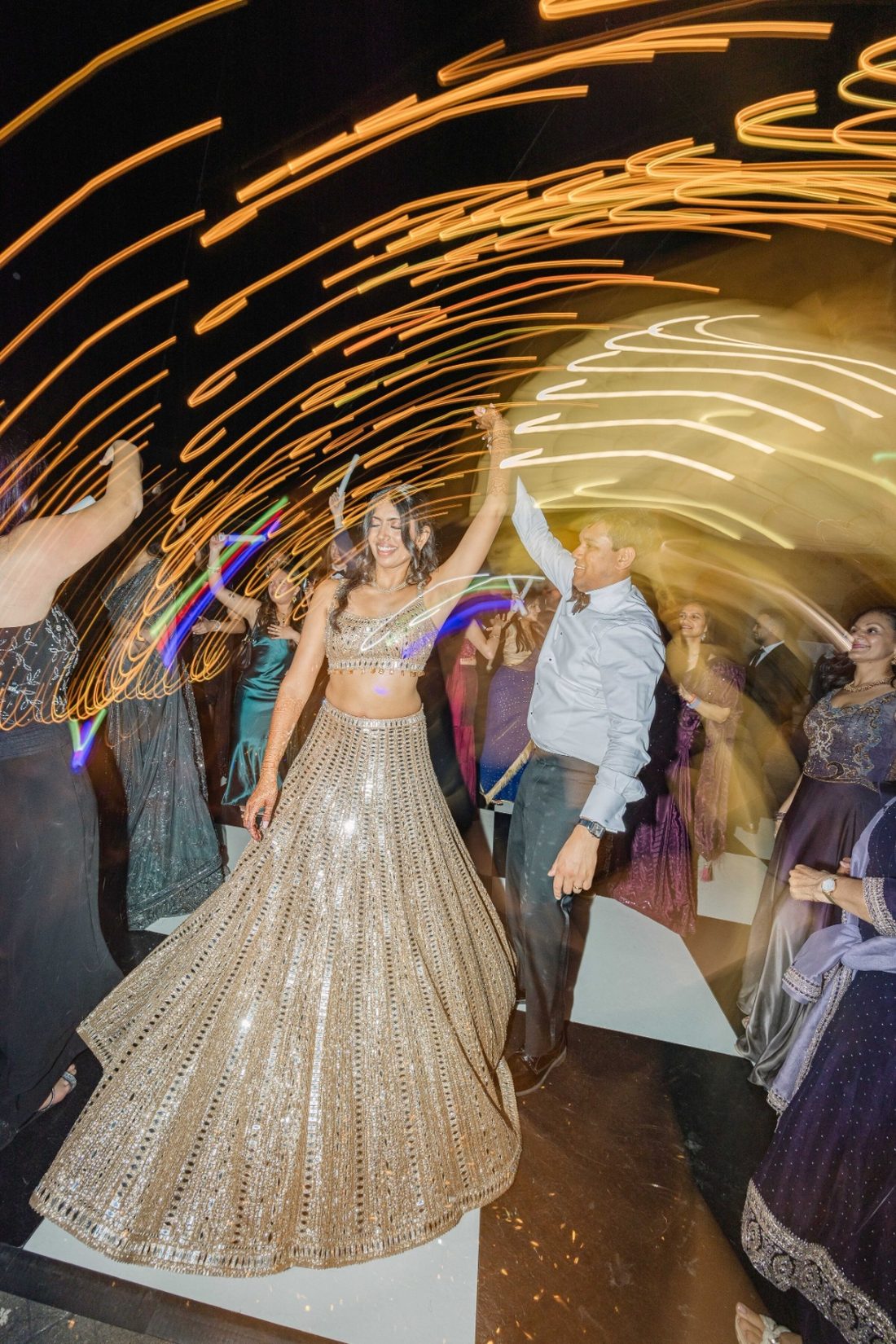 Bride twirling in a gold lehenga under swirling reception lights with her father