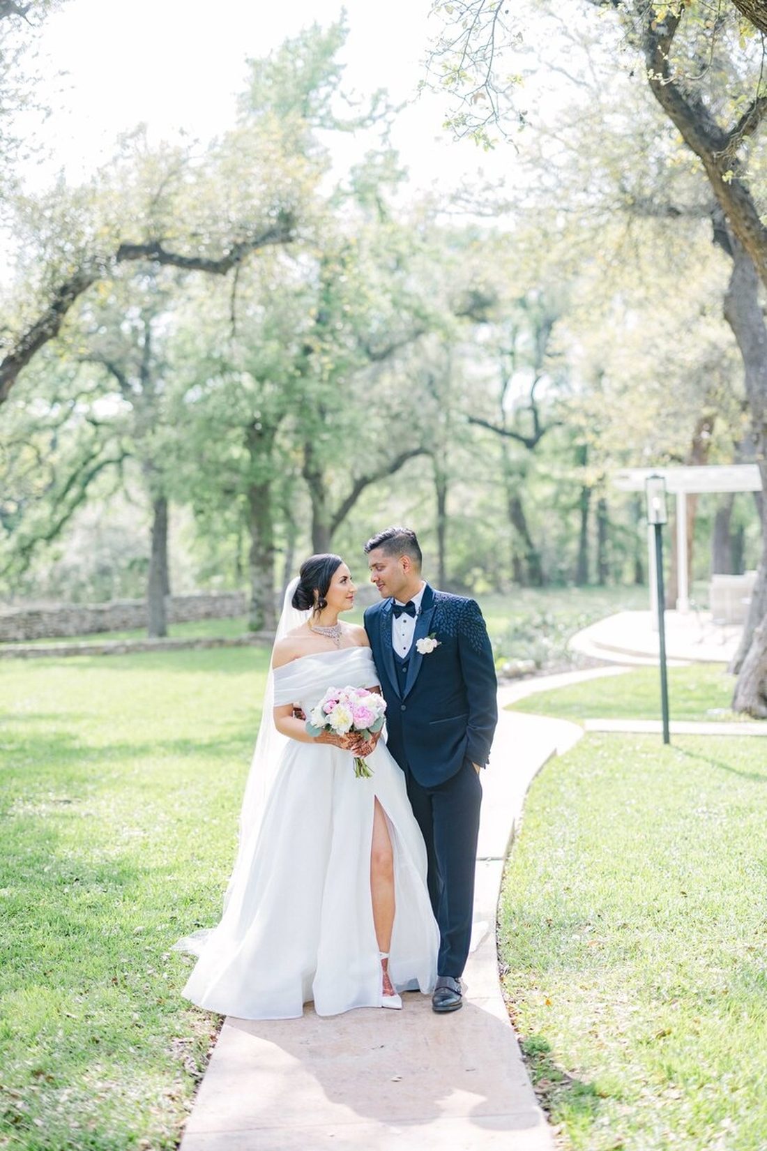 Bride and groom sharing a smile on a stone pathway during their first look