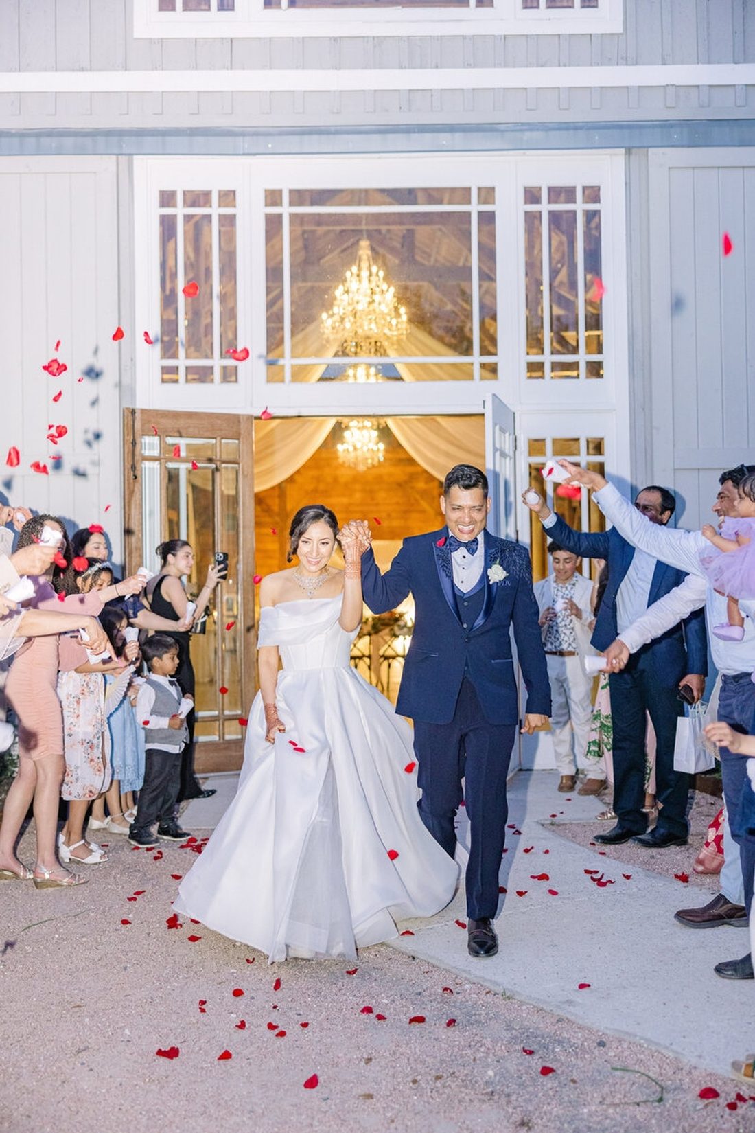 Couple walking hand-in-hand through a shower of red rose petals at their grand exit