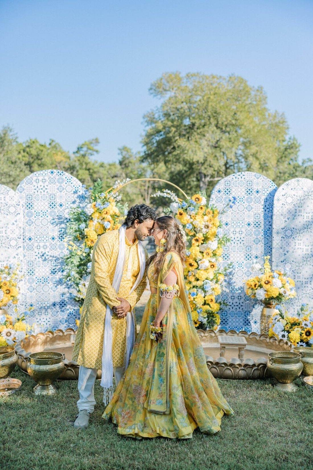 Couple dressed in yellow standing nose-to-nose at a sunlit haldi mandap