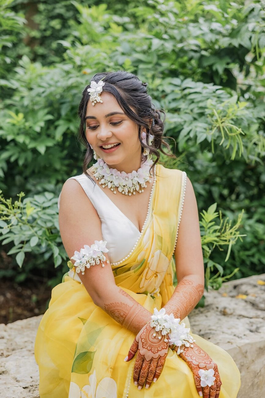 Bride in yellow saree with floral jewelry, mehndi hands