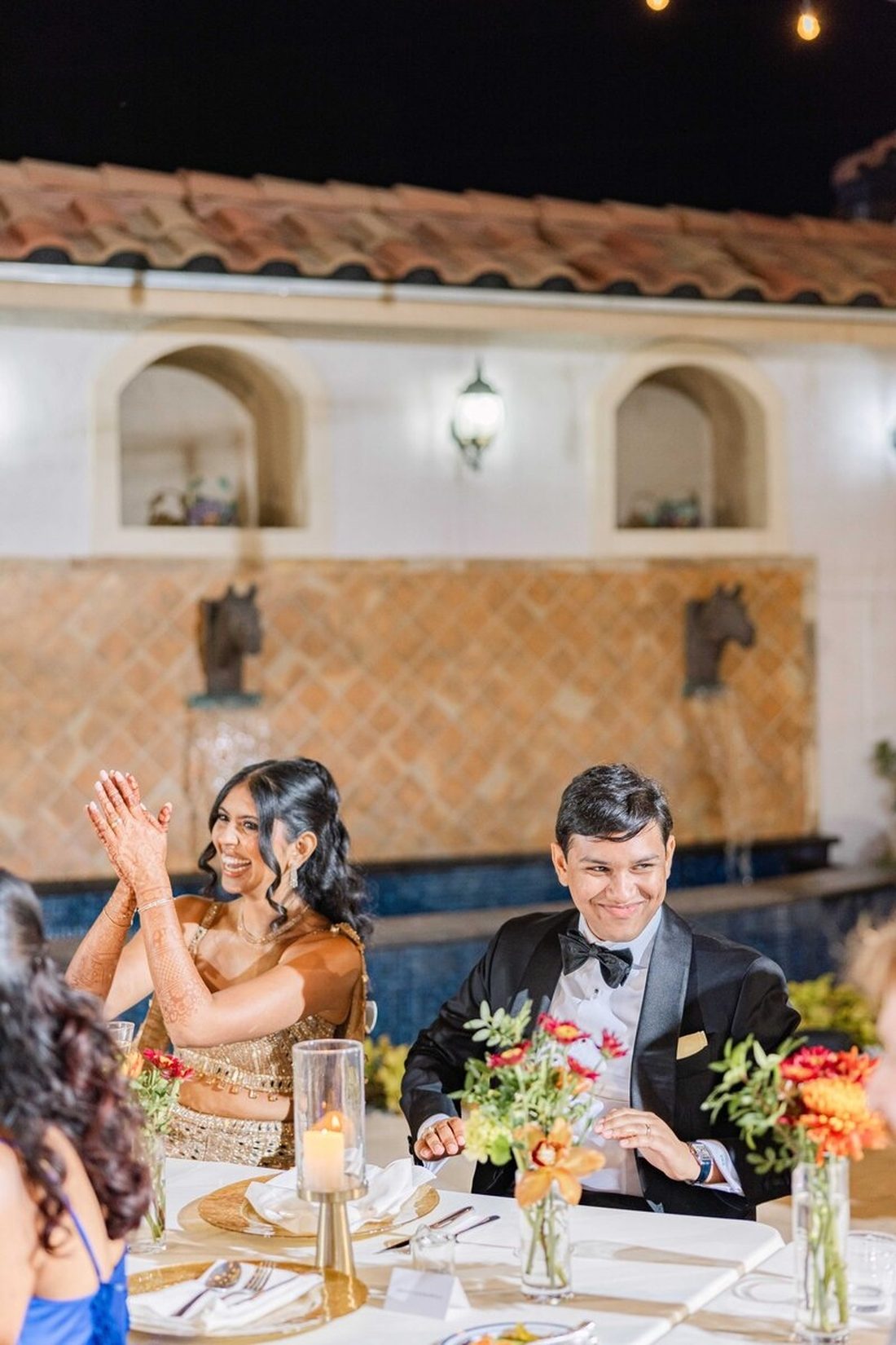 Bride clapping and groom smiling beside her at the reception sweetheart table